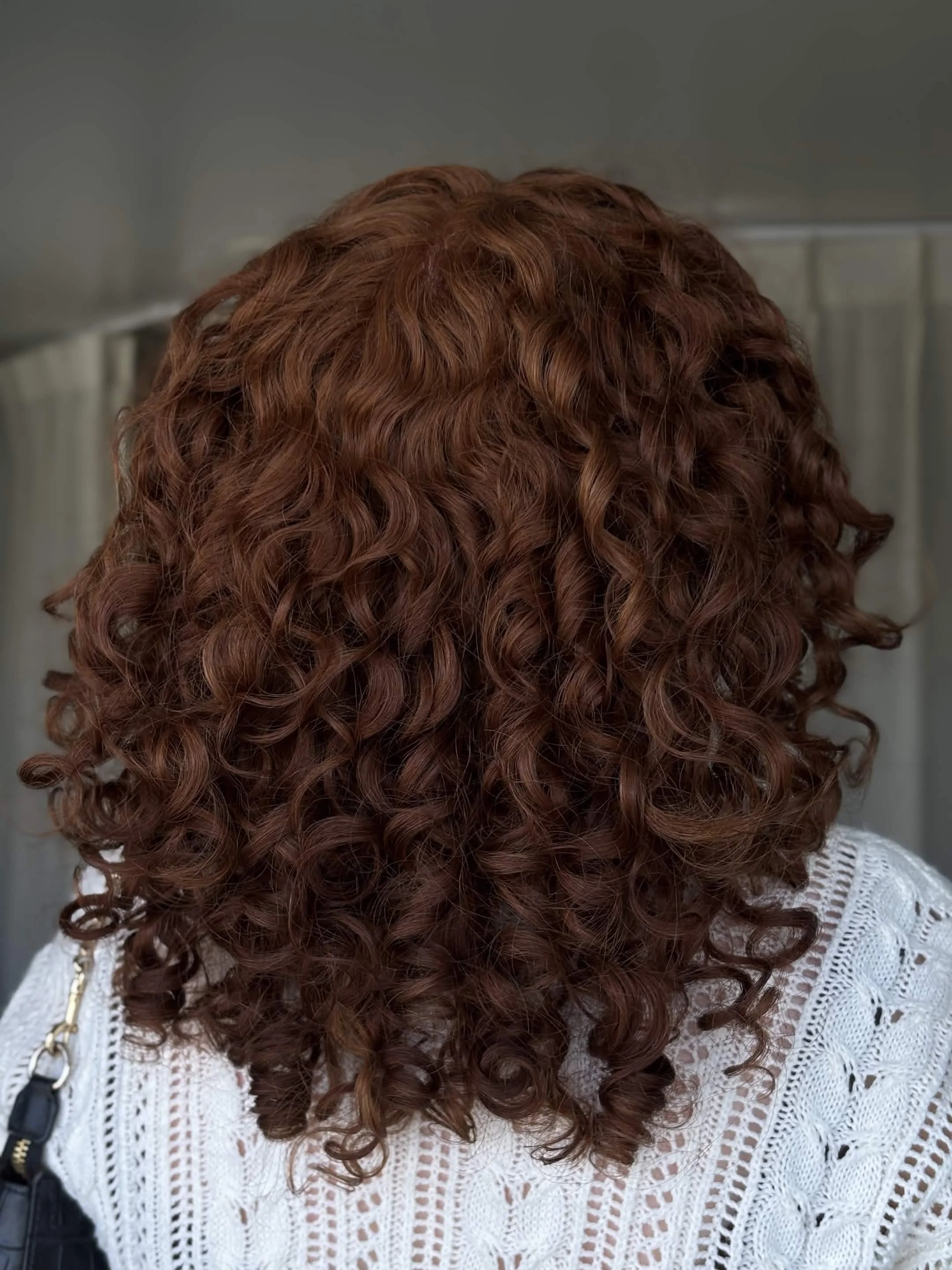 Person with curly reddish-brown hair wearing a white crocheted top and carrying a black purse.
