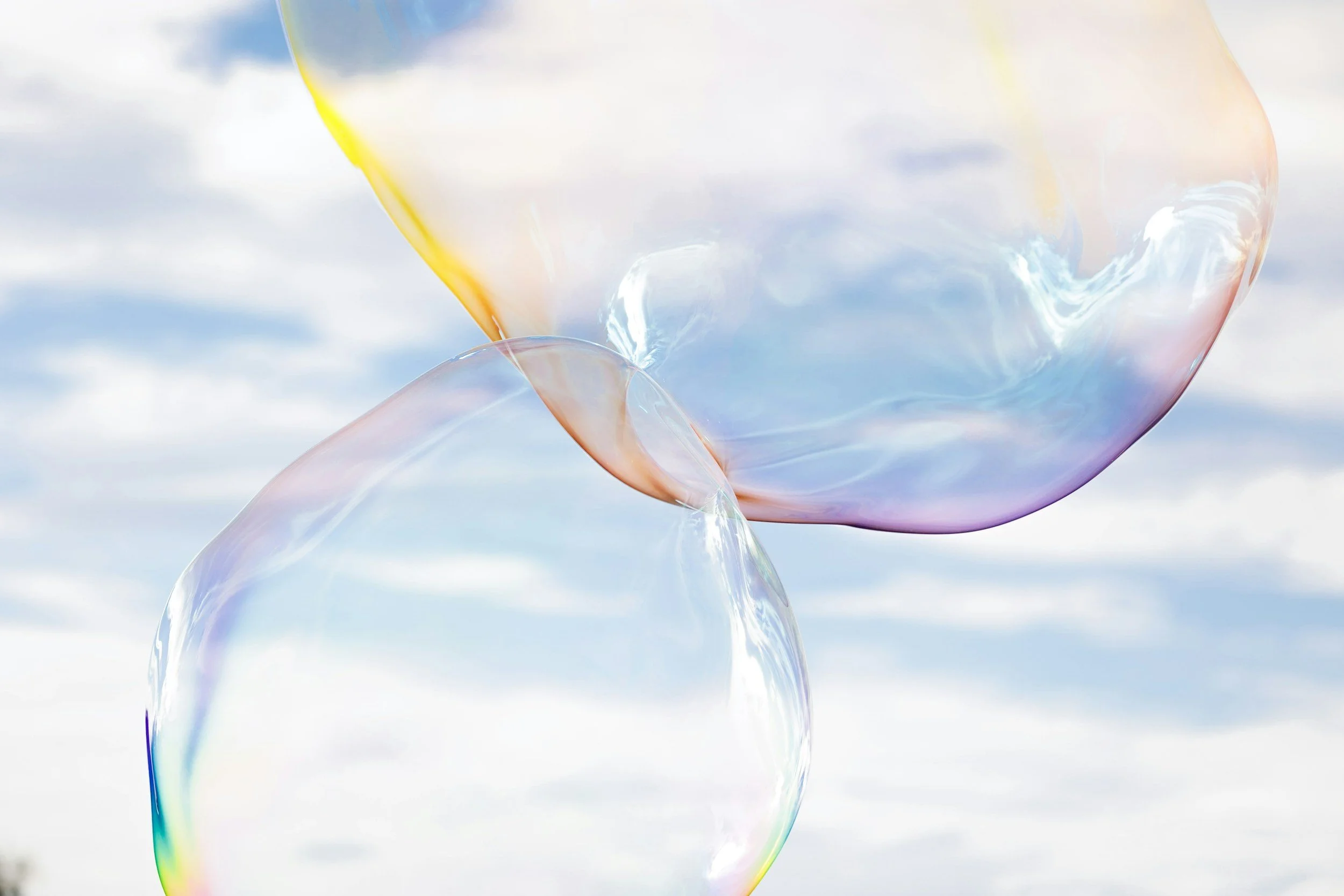 Close-up of two iridescent soap bubbles connecting against a cloudy sky.