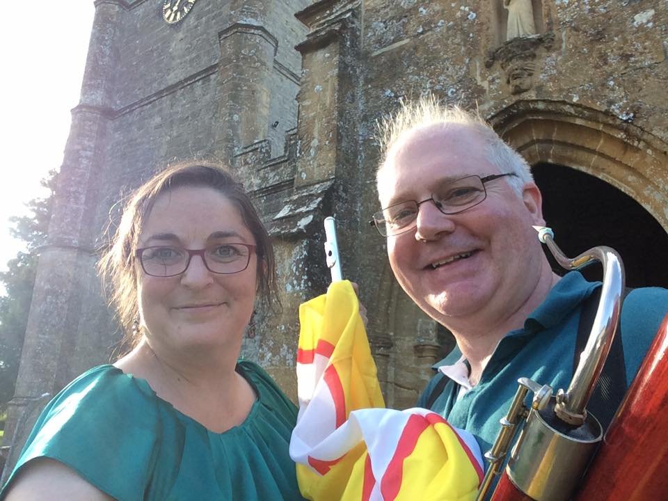 Katy and Miles outside Bradford Abbas Church with Dorset flag and instruments