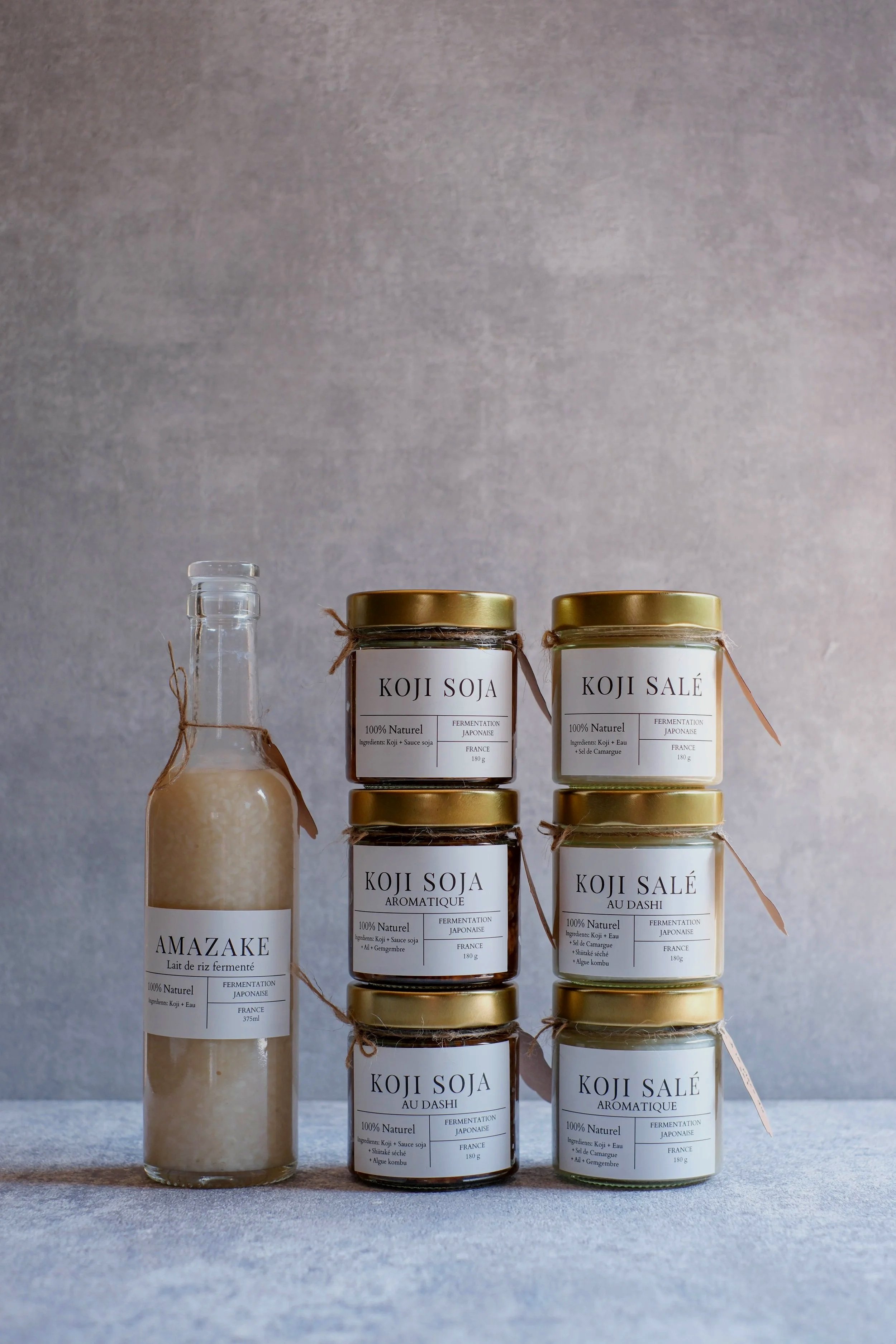 Gamme de produits fermentés japonais, notamment du soja, de l'amedzaké, et du salé au dashi, présentés dans des bocaux et une bouteille en verre, avec une étiquette minimaliste.