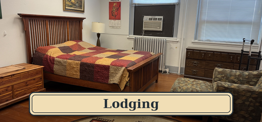 A cozy motel room with a wooden bed frame, a colorful patchwork quilt, a nightstand with a lamp, an air conditioning unit in the window, a vintage dresser, and a patterned armchair. Blue Mountain Creation Retreat