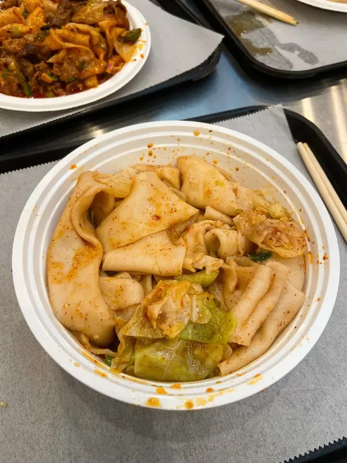 Thick, hand-ripped flat noodles coated in red chili oil inside a takeout bowl.