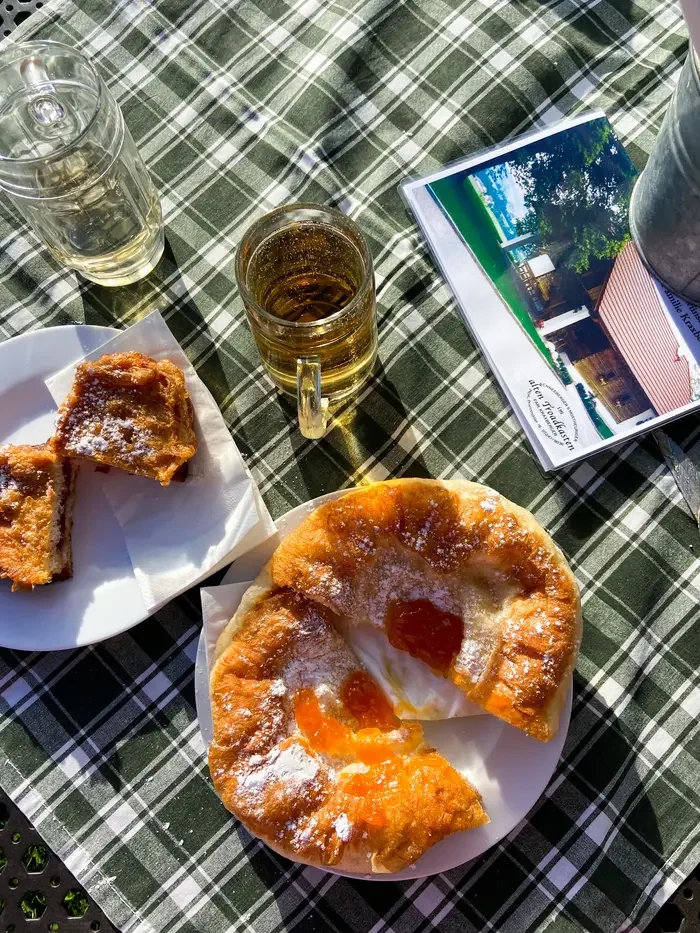 Traditional Austrian pastries dusted with powdered sugar on white plates, served alongside glasses of apple juice on a green-and-white checkered tablecloth.