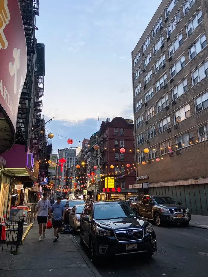 Colorful paper lanterns and string lights hanging over a street in Chinatown at dusk.