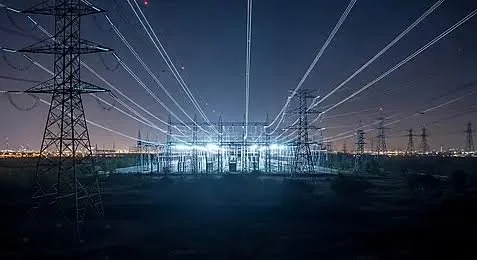 Nighttime view of electrical power lines and pylons with light beams radiating from a central structure.
