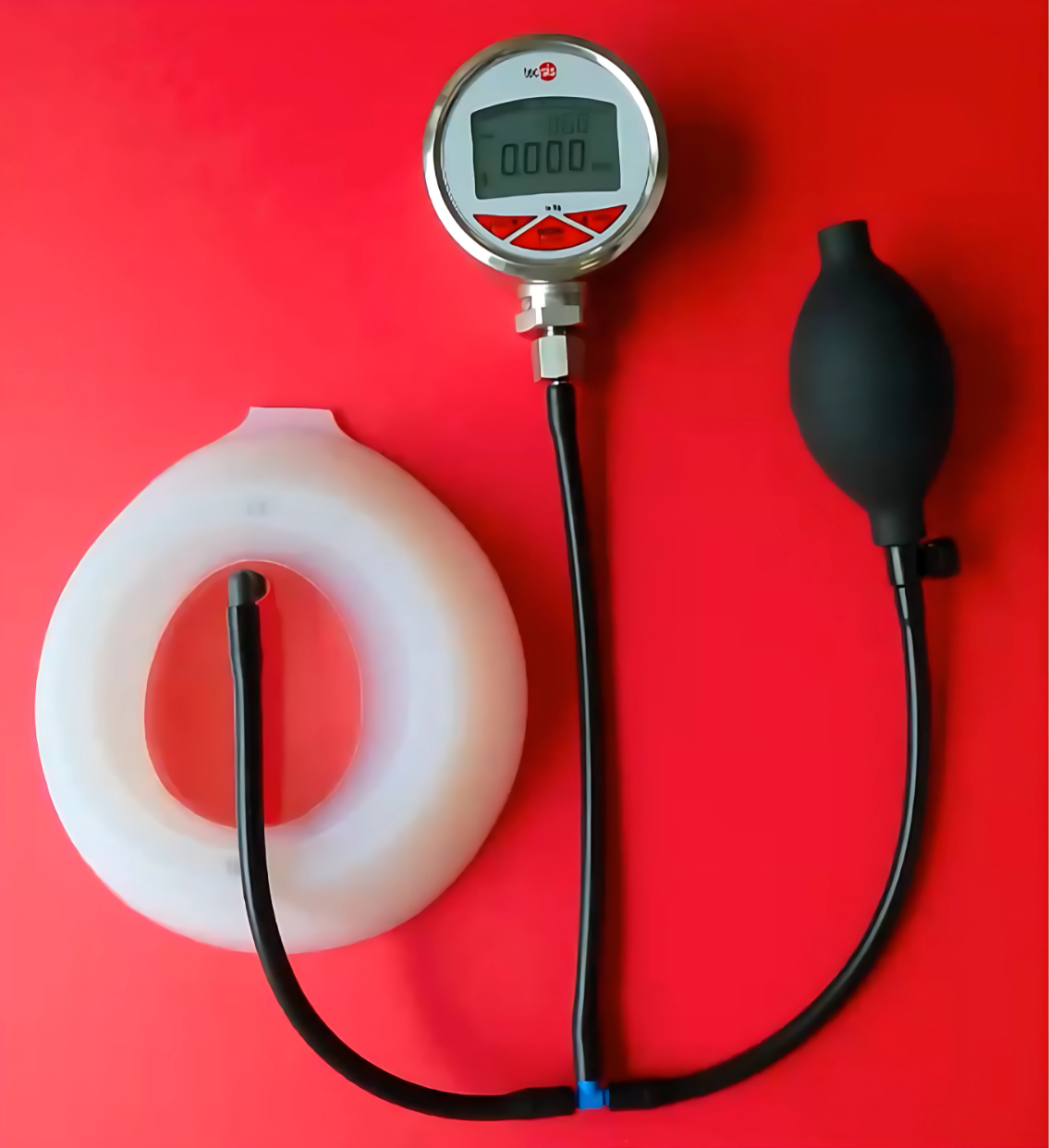 A medical digital manometer connected to a black rubber balloon and a white silicone ring on a red background.