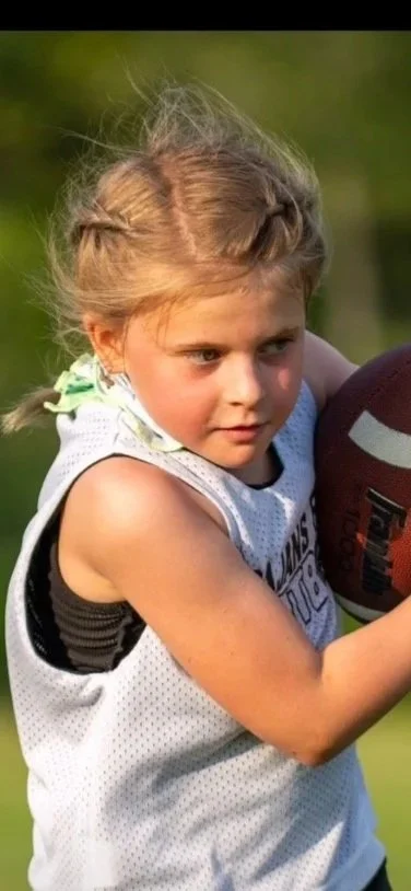 Young girl with blonde hair holding a football during a football practice or game