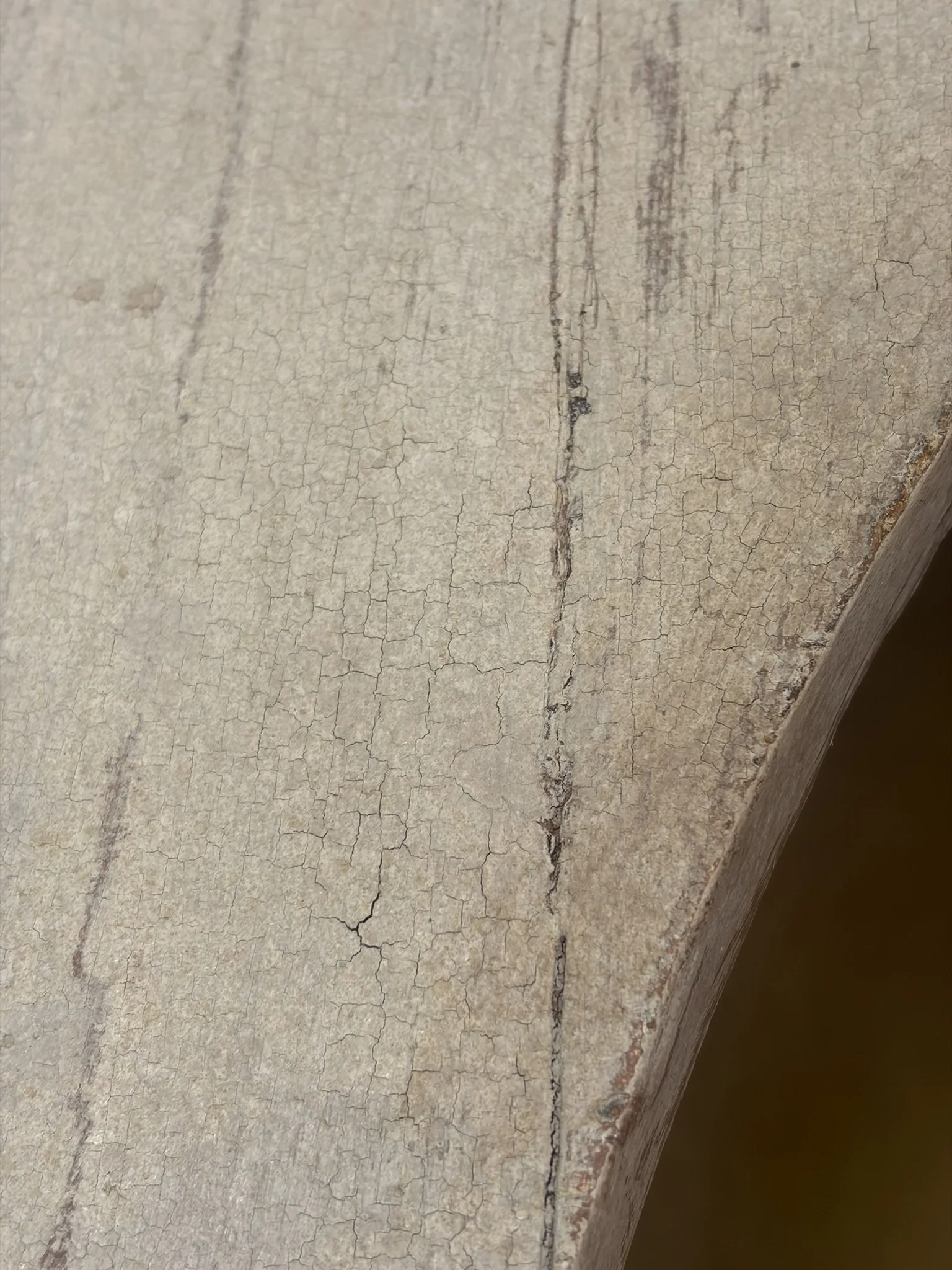 Superficie di un muro con vernice screpolata e crepe, visibile anche un bordo in legno.