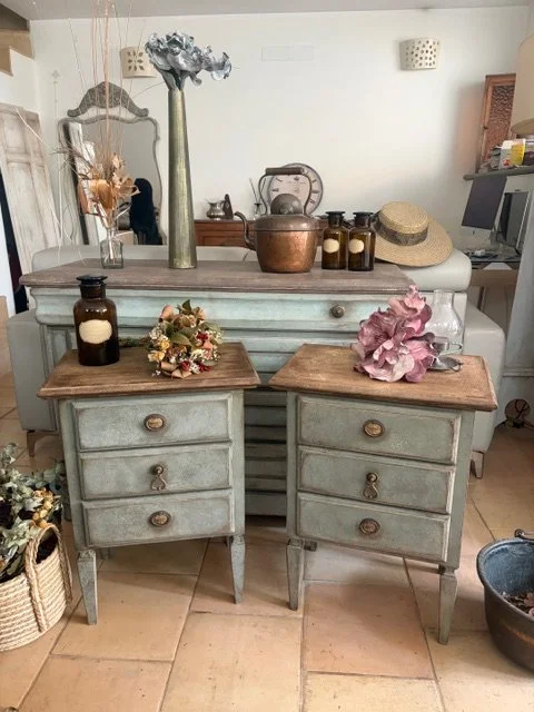 Due vecchie comodini di colore azzurro con cassetti in legno naturale, decorati con fiori secchi e bottiglie di vetro, posizionati in un ambiente rustico. Sul piano più alto ci sono altri oggetti decorativi e barattoli in vetro.