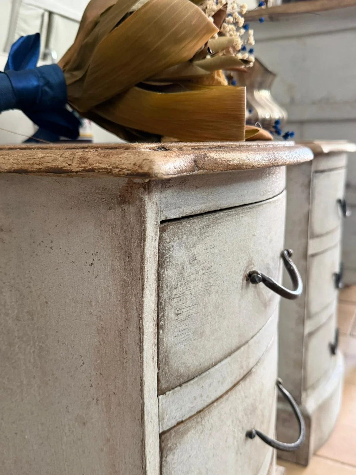 Cassetti di un mobile antico in legno verniciato di bianco con maniglie metalliche nere, sopra una superficie di legno naturale.
