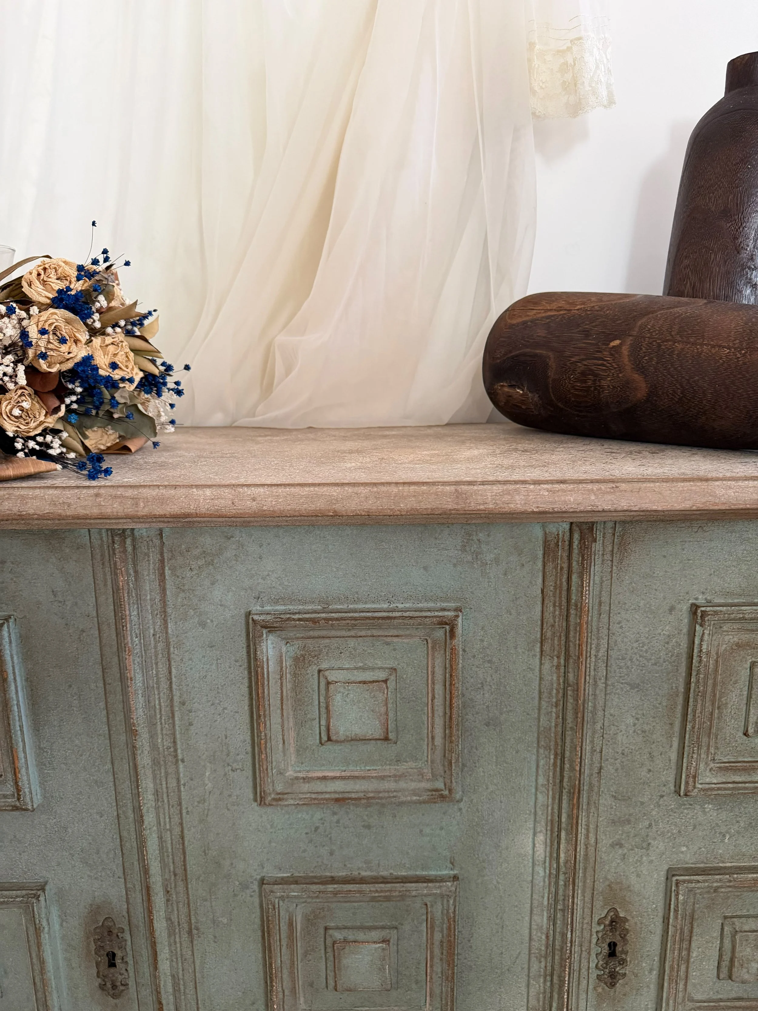 Una credenza antica color verde con decorazioni in rilievo, un'anta con maniglie in ottone e un vetro trasparente