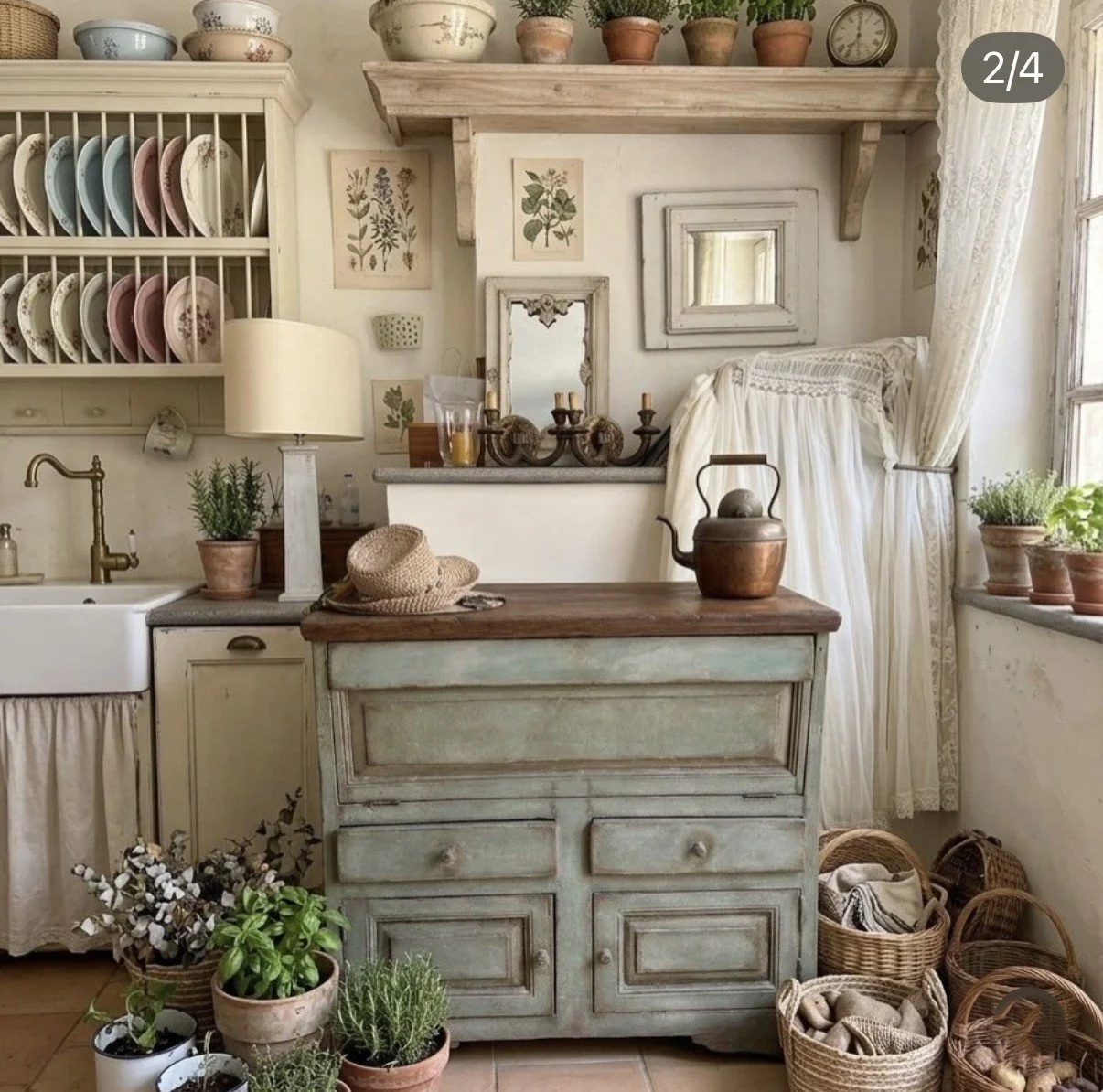 Interno di una cucina rustica con mobili vintage, piatti esposti, piante in vaso e oggetti decorativi in stile campagna.