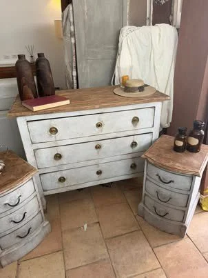 Cassettiera bianca con piano in legno e vari oggetti decorativi, come vasi, libri e bottiglie, in un ambiente domestico.