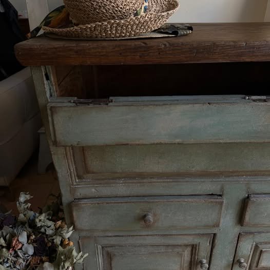 Vecchio mobile in legno con cassetti, sopra un piano in legno, con un cesto di paglia sul piano.