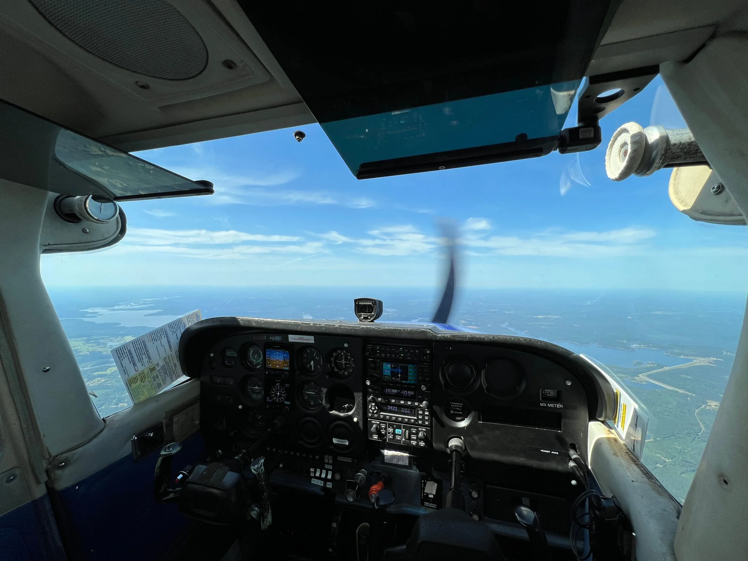 Cockpit of an airplane flying high above the landscape with a clear blue sky and scattered clouds.