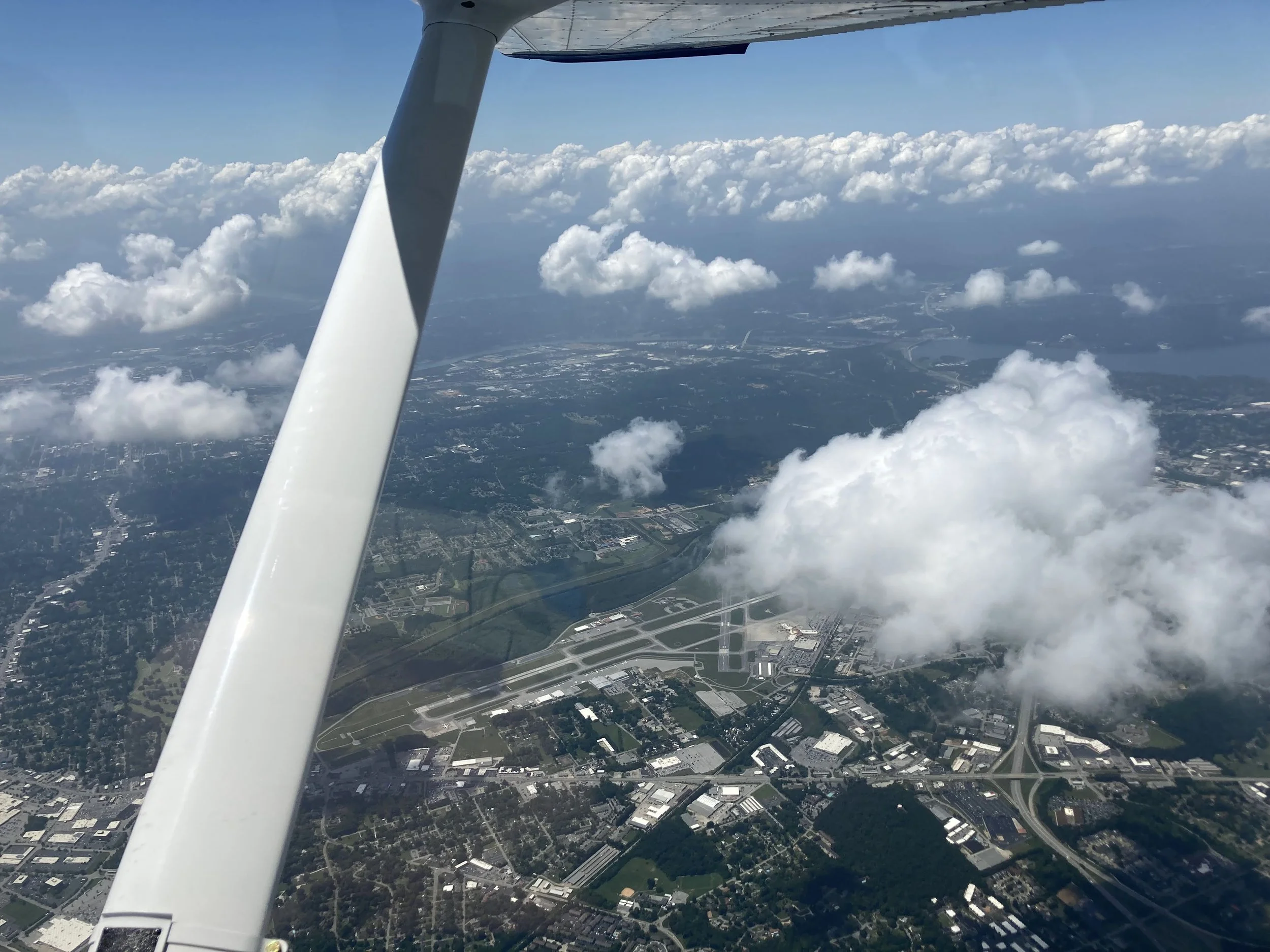 View from an airplane showing the wings, clouds, and a cityscape below