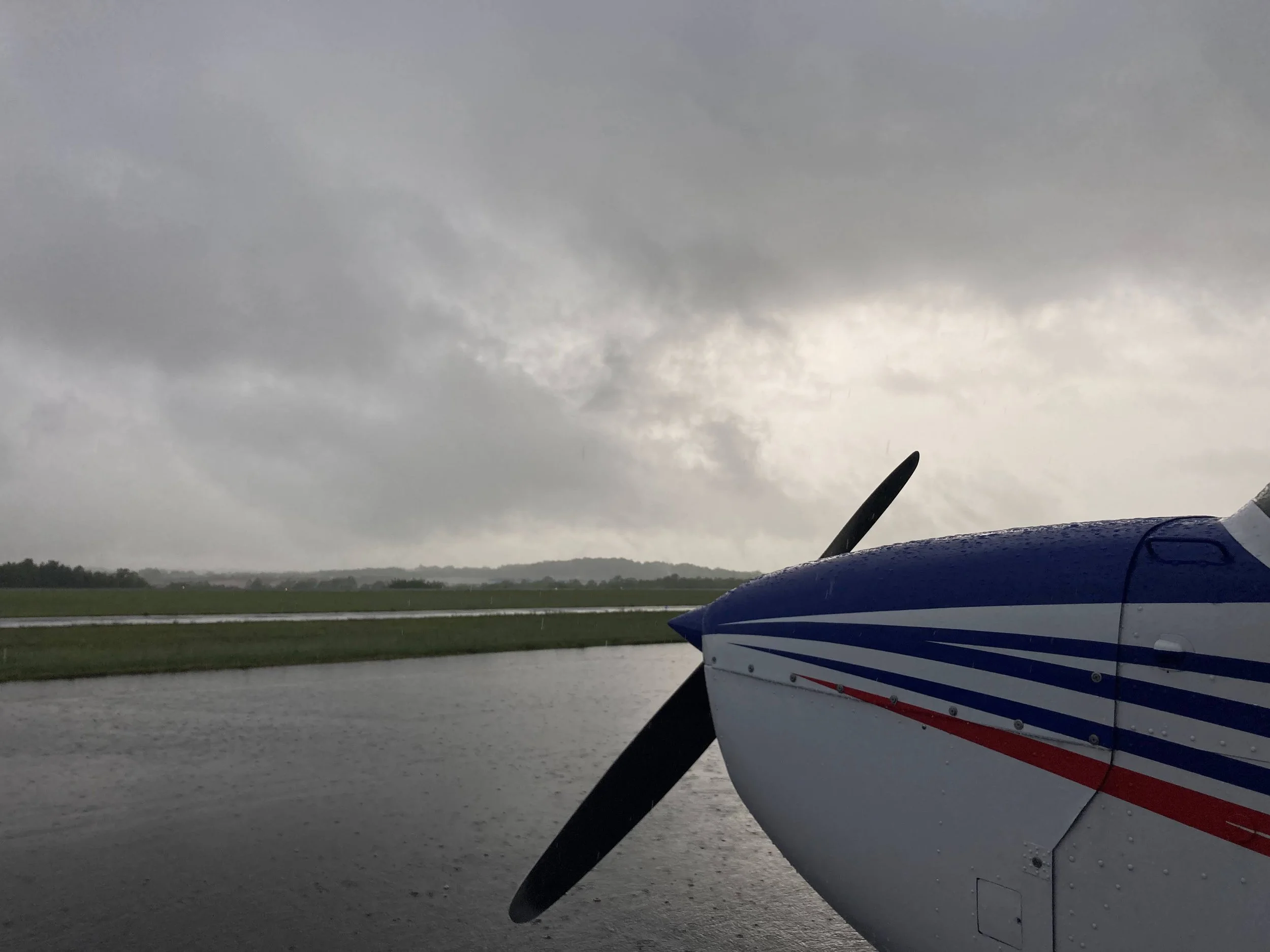 Part of an airplane with a red, white, and blue striped design, parked near a body of water under a cloudy sky.