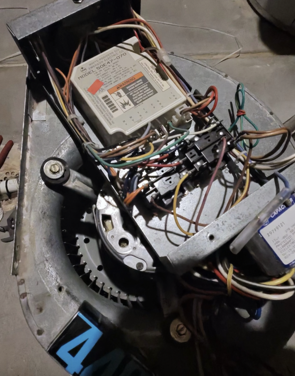 The image shows the internal components of an electric motor, including a circuit board, wiring, and a label with safety warnings.
