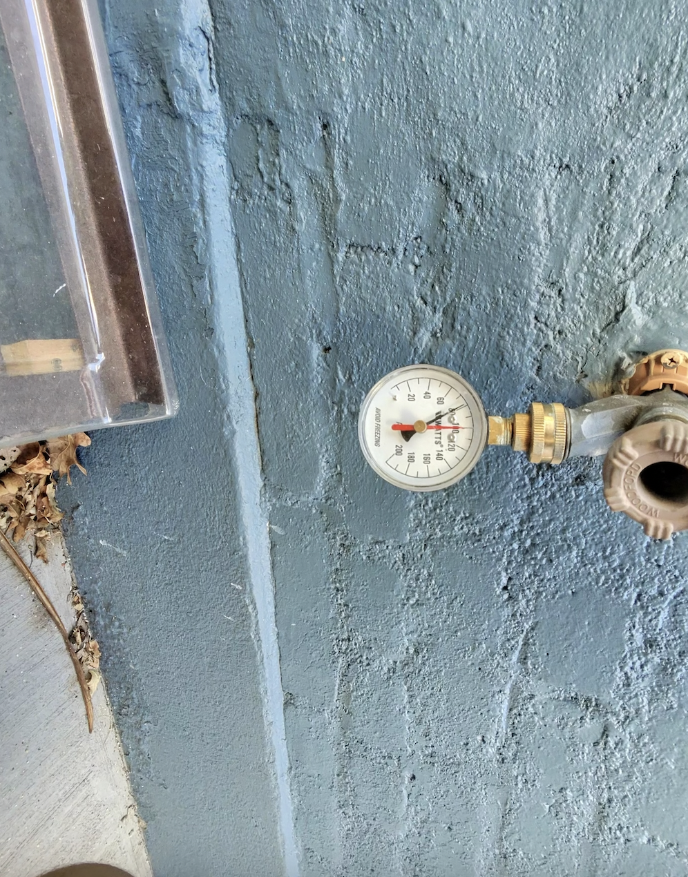 A pressure gauge attached to a water pipe on a blue wall, indicating around 60 psi pressure.