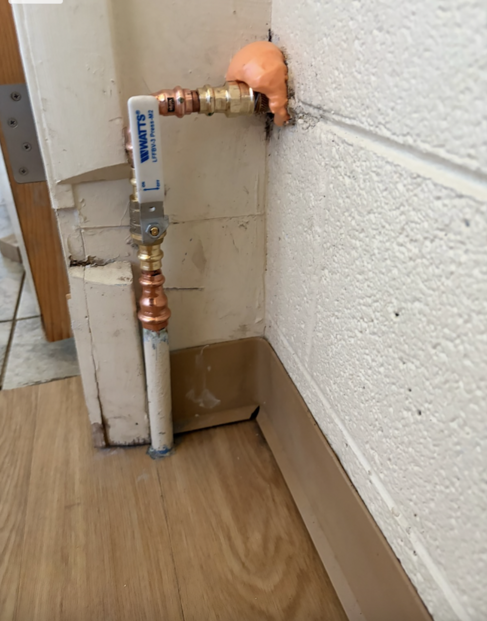 Warm water valve connected to copper pipes on a kitchen or laundry room wall with insulation foam around it.