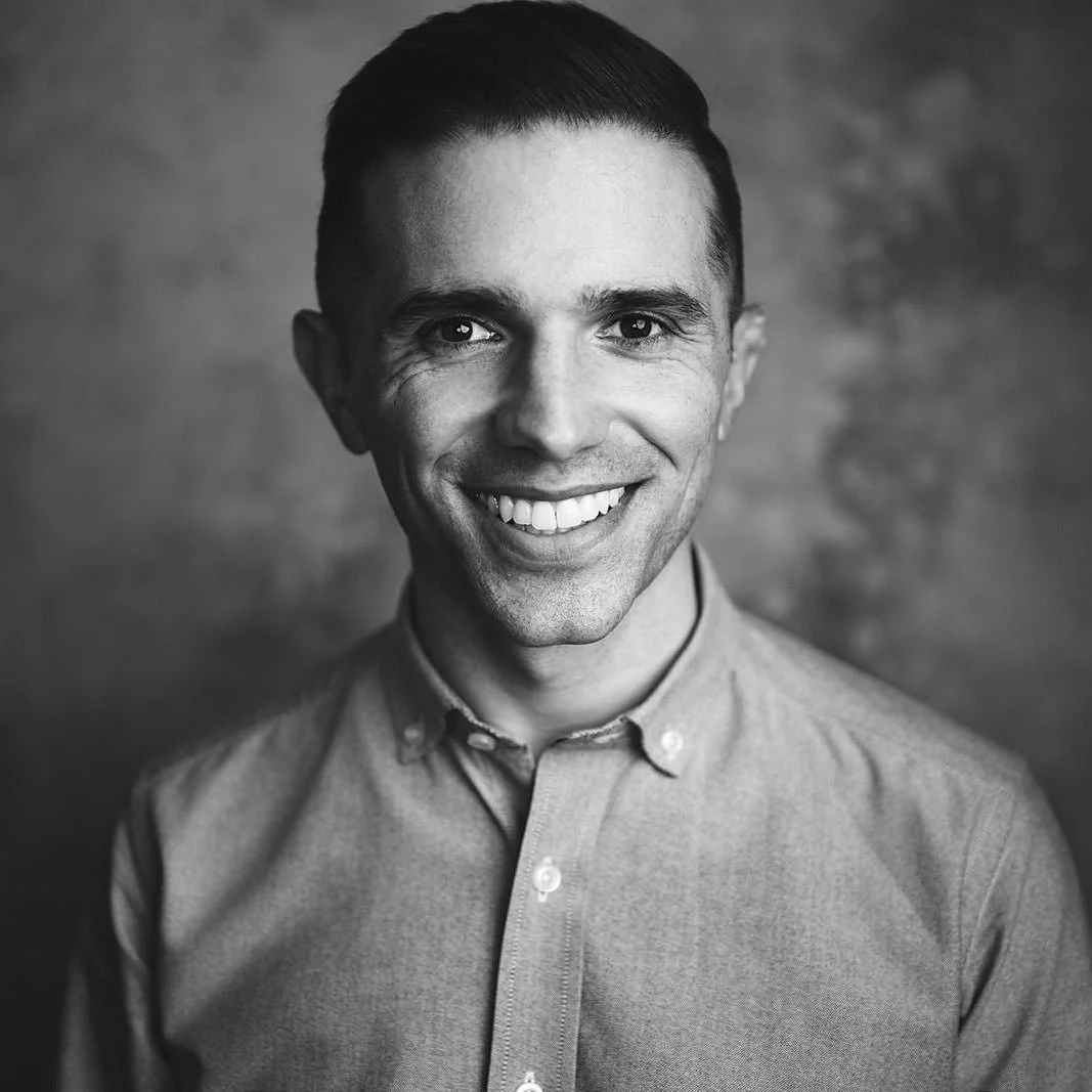 young man smiling warmly for the camera in a black and white headshot photo