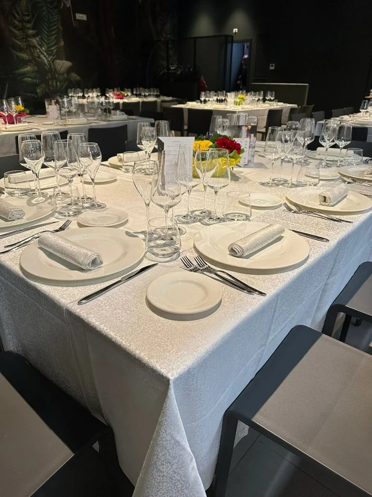 Tavolo da banchetto elegantemente apparecchiato con tovaglia bianca, piatti, posate, bicchieri e centrotavola floreale