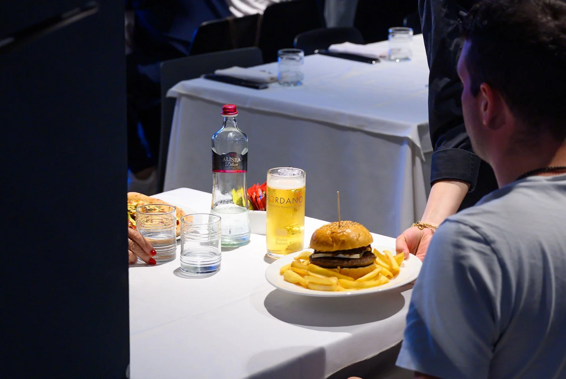 Tavolo apparecchiato con hamburger e patatine, birra, acqua e bicchieri in un ristorante.