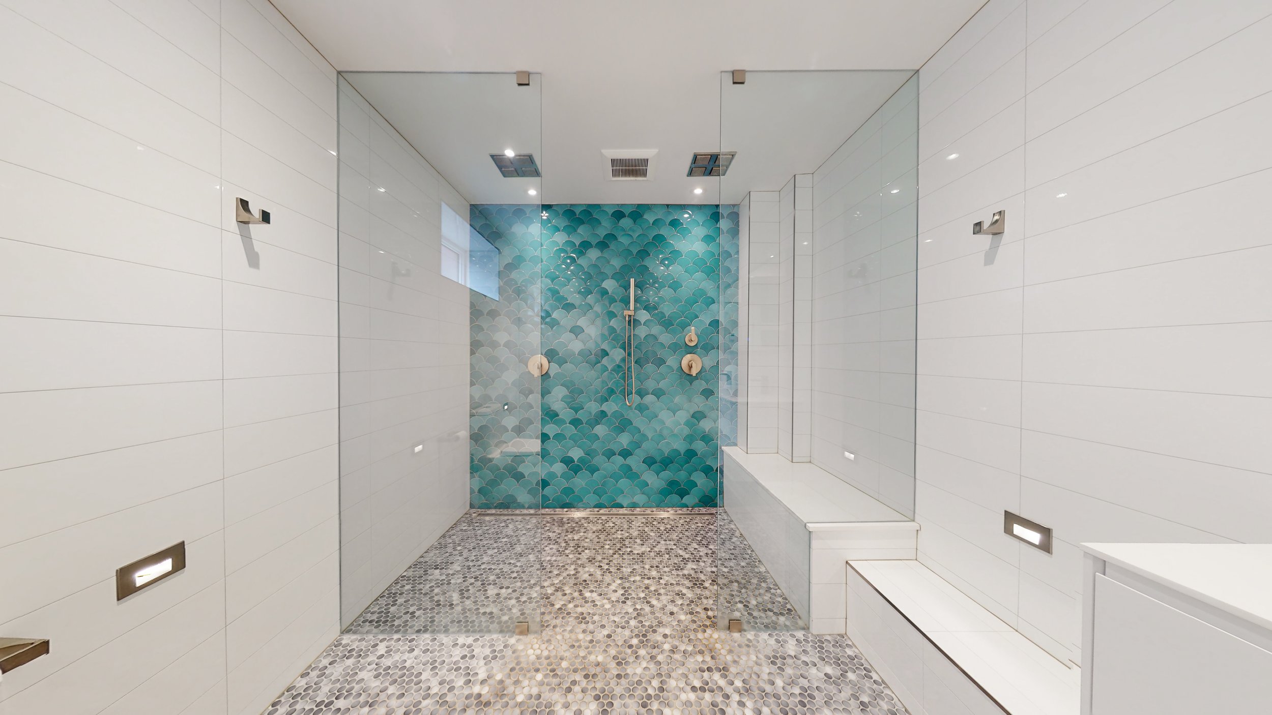 Modern walk-in shower with glass doors, teal fish scale tile accent wall, and pebble stone floor.