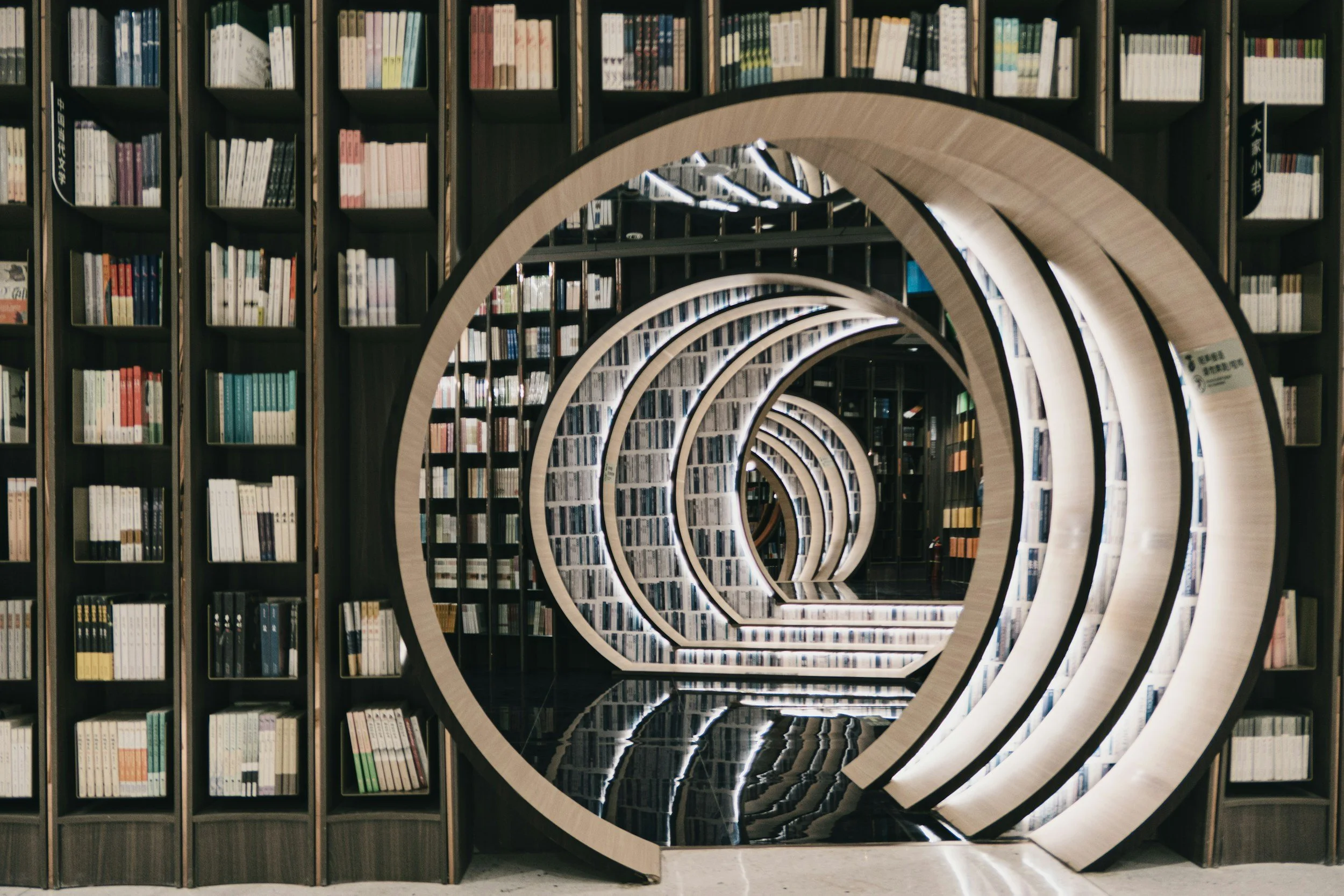 A modern library with bookshelves and a spiral staircase with circular openings, creating a tunnel-like effect.