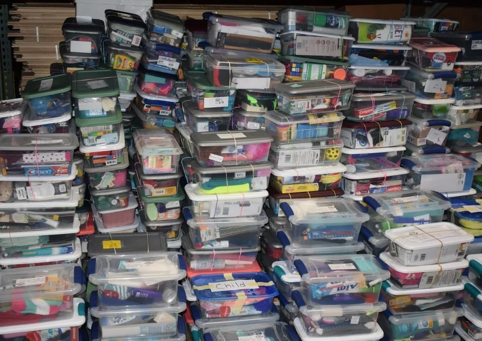 Stacks of clear plastic storage containers filled with various school supplies, organized in rows on shelves.