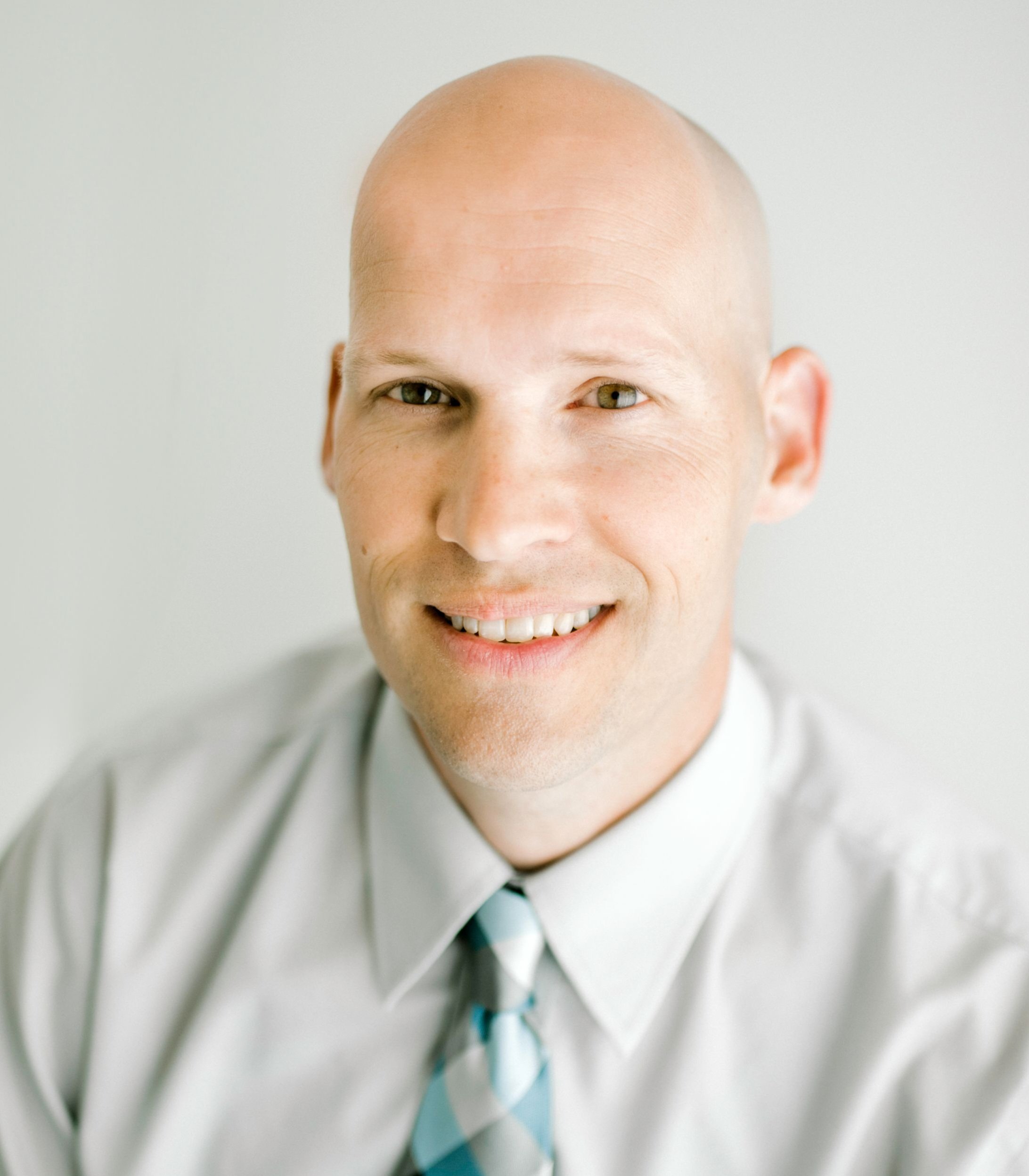 Close-up of a smiling bald man wearing a light-colored suit and light blue tie.
