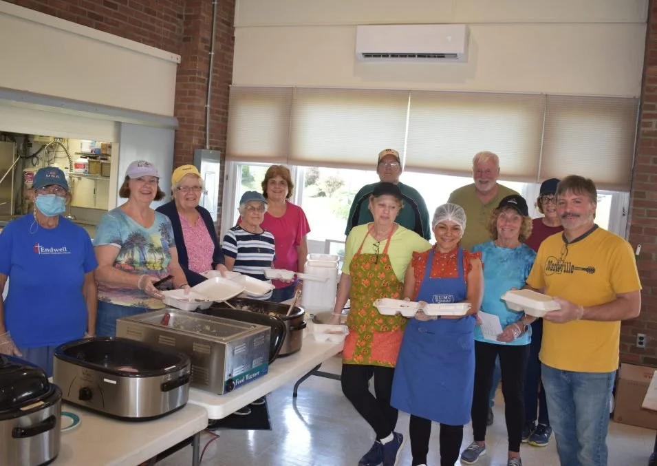 Group of people preparing and distributing food in a community center or kitchen.