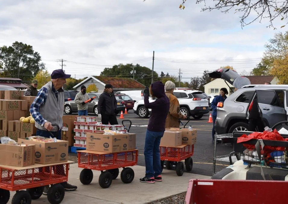 People at a food bank distributing boxes of food and groceries in a parking lot.