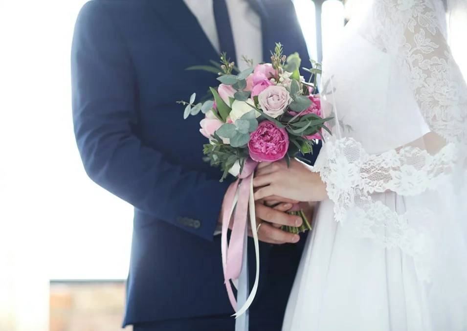Bride and groom holding a bouquet of pink and white flowers during their wedding.