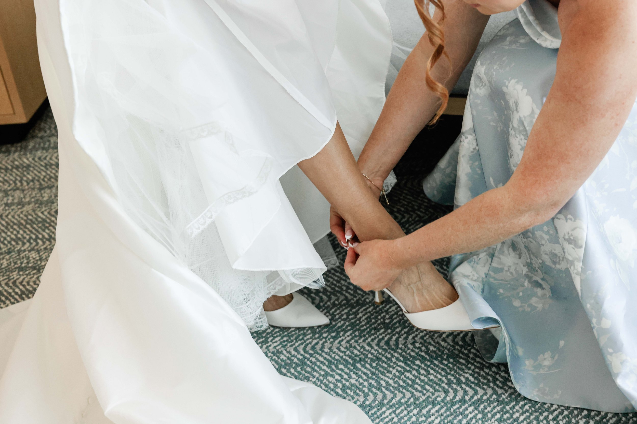 A bride in a white wedding dress holding hands with a woman in a blue floral dress.