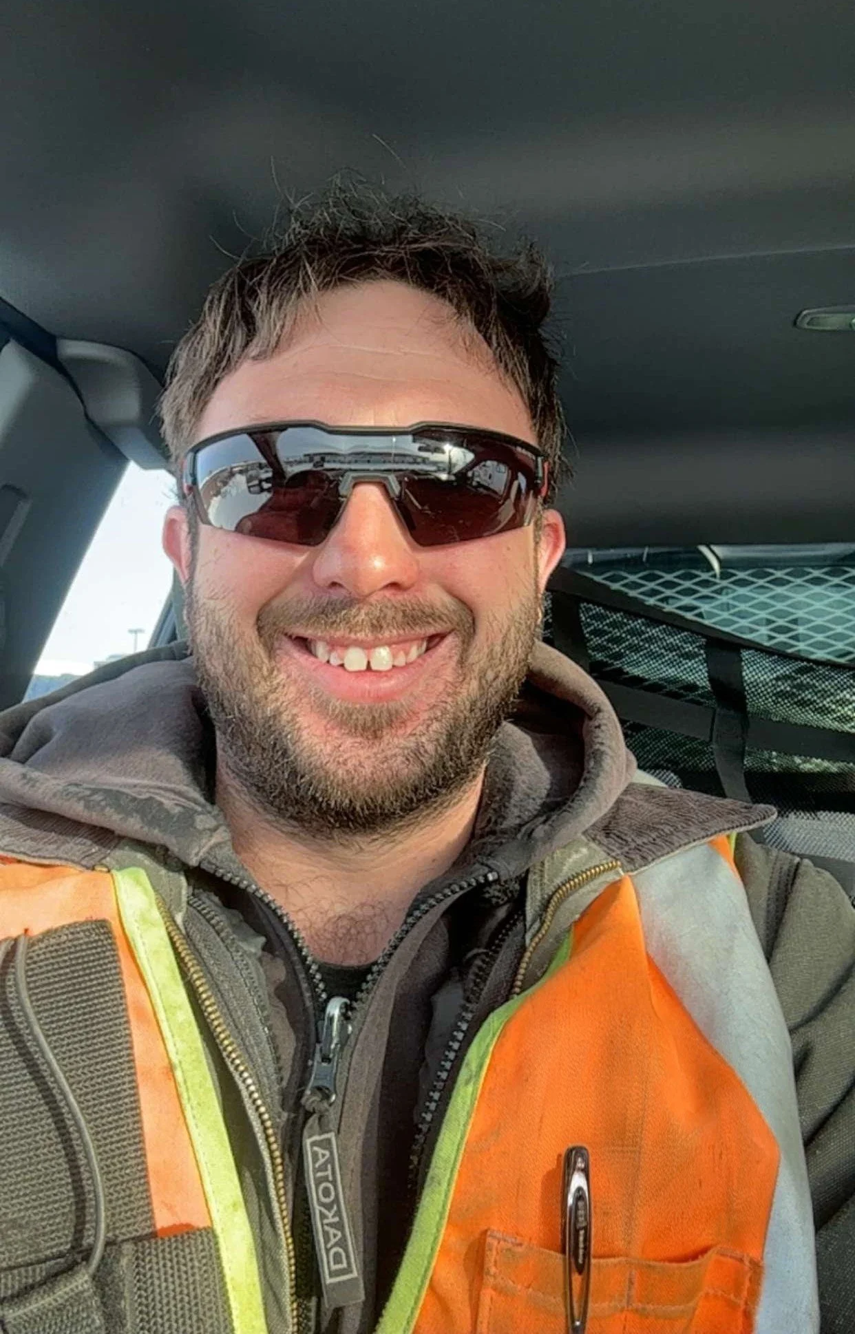 A smiling man wearing sunglasses and work safety vest inside a vehicle. Phil Gauthier, septic inspector for Spotlight Home Inspections.