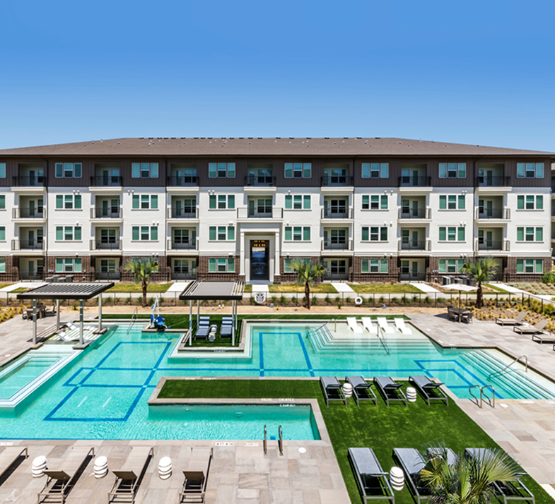 Modern apartment complex with a swimming pool area, lounge chairs, palm trees, and a blue sky.