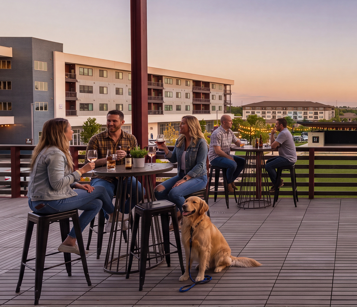 Five people and a dog on a patio at sunset, socializing with drinks.