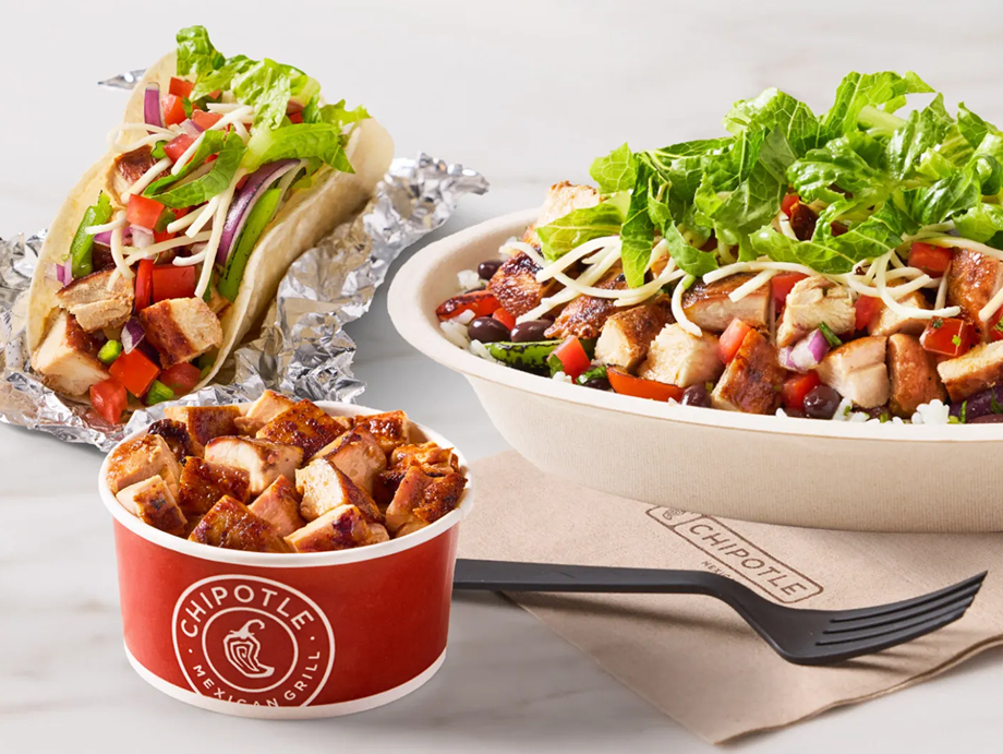 A salad with lettuce, grilled chicken, tomatoes, shredded cheese, and croutons in a bowl, a taco with lettuce, tomatoes, shredded cheese, grilled chicken, and foil-wrapped shell, and a small cup of grilled chicken pieces, all from Chipotle Mexican Grill.