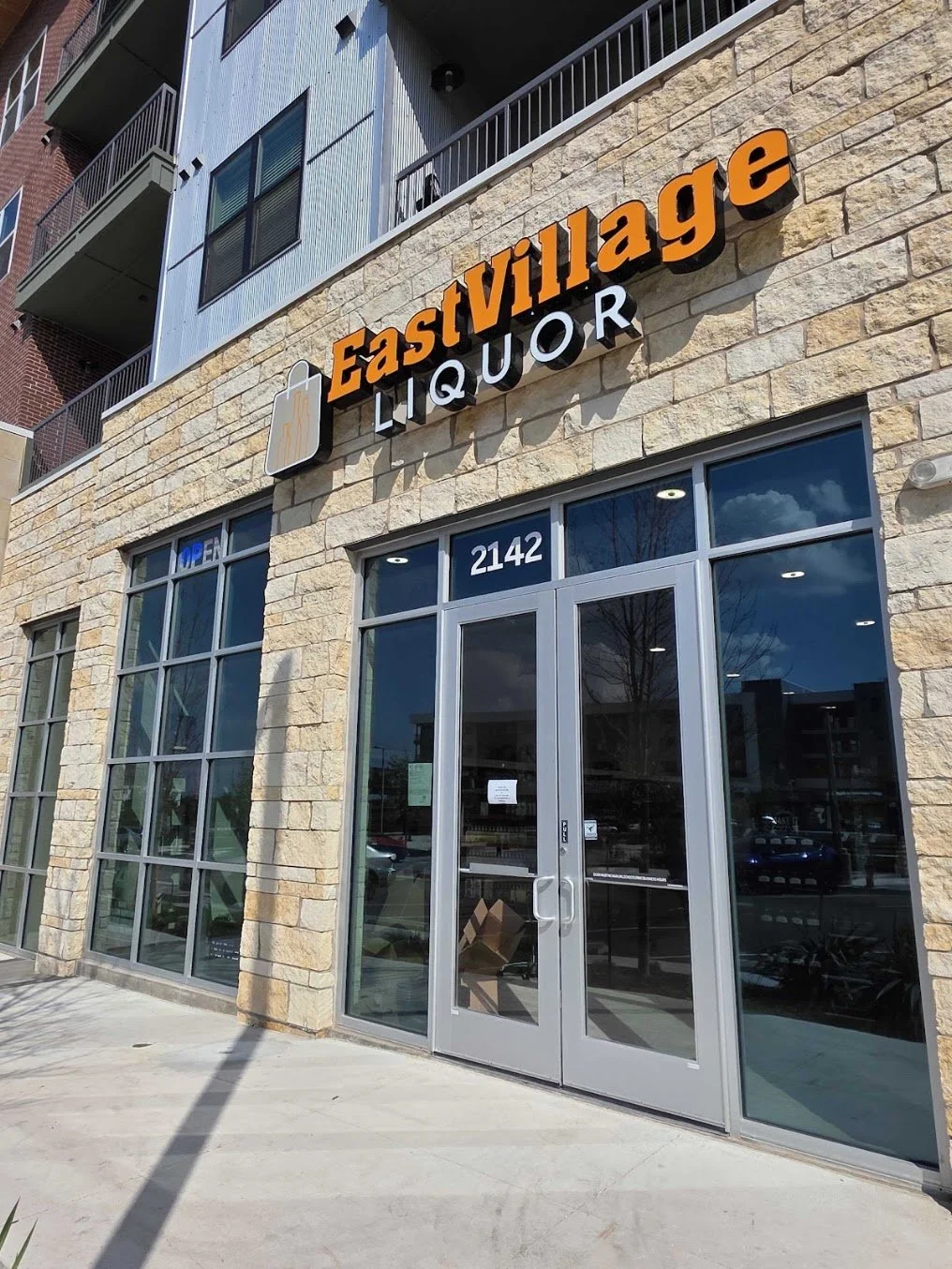 Exterior view of Eastivillage Liquor store with stone facade, glass double doors, and signage including a beer mug logo.
