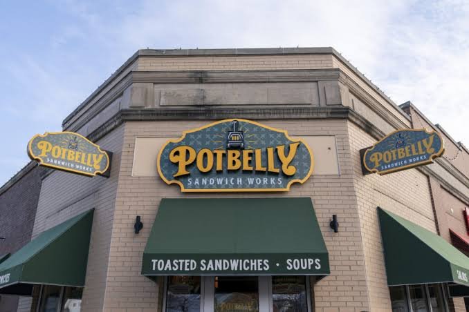 Exterior of Potbelly Sandwich Works restaurant with green awnings and signage advertising toasted sandwiches and soups.