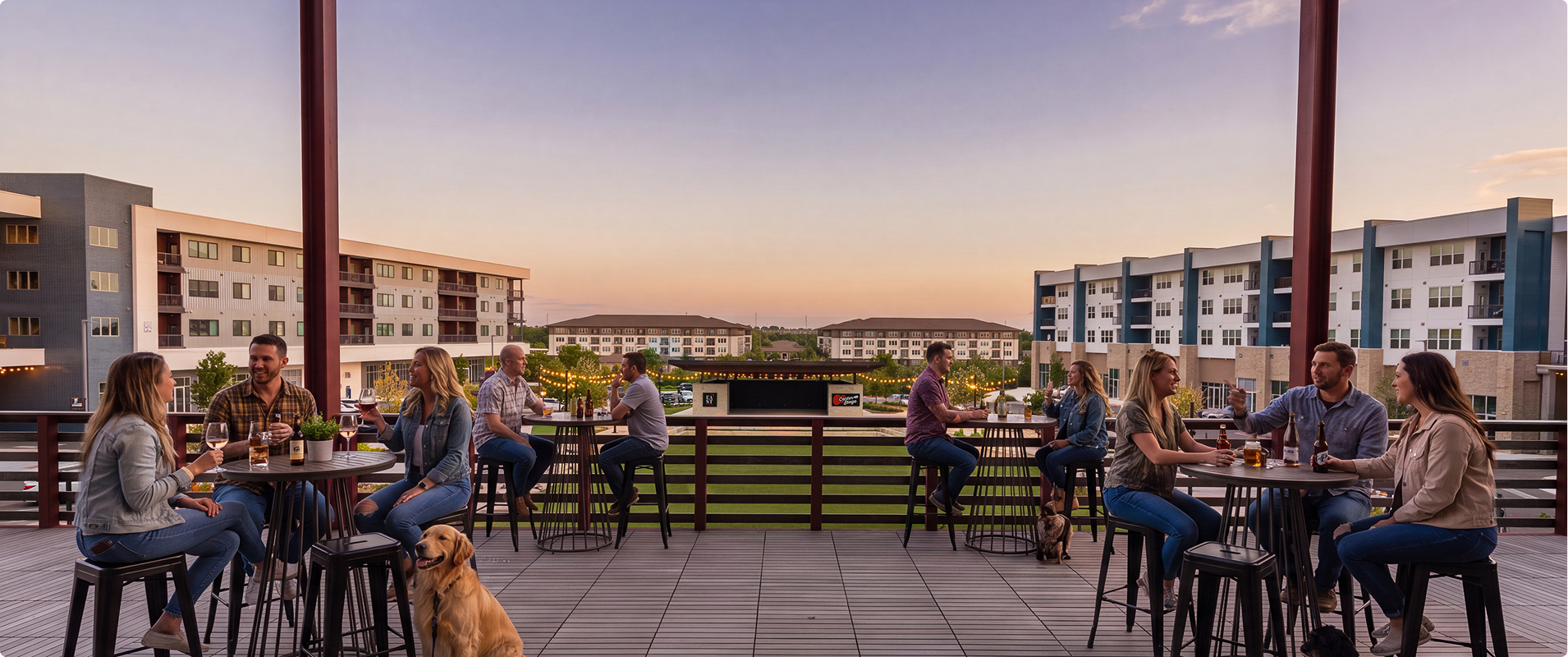 People socializing on a balcony at sunset, sitting around tables with drinks, with modern apartment buildings in the background.
