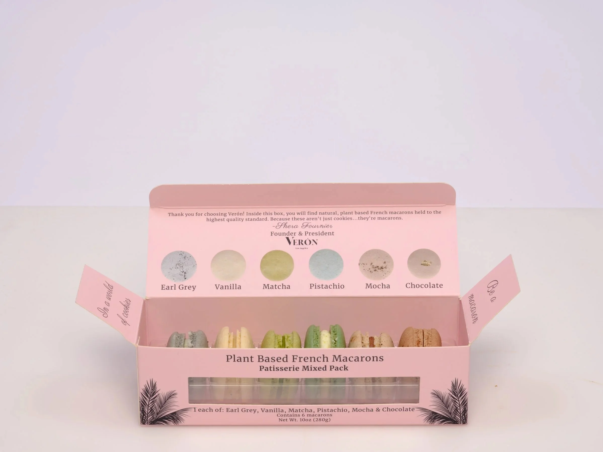 Open pink box of plant-based French macarons with labeled flavors: Earl Grey, Vanilla, Matcha, Pistachio, Mocha, and Chocolate, with a note thanking the customer and details about the macarons.
