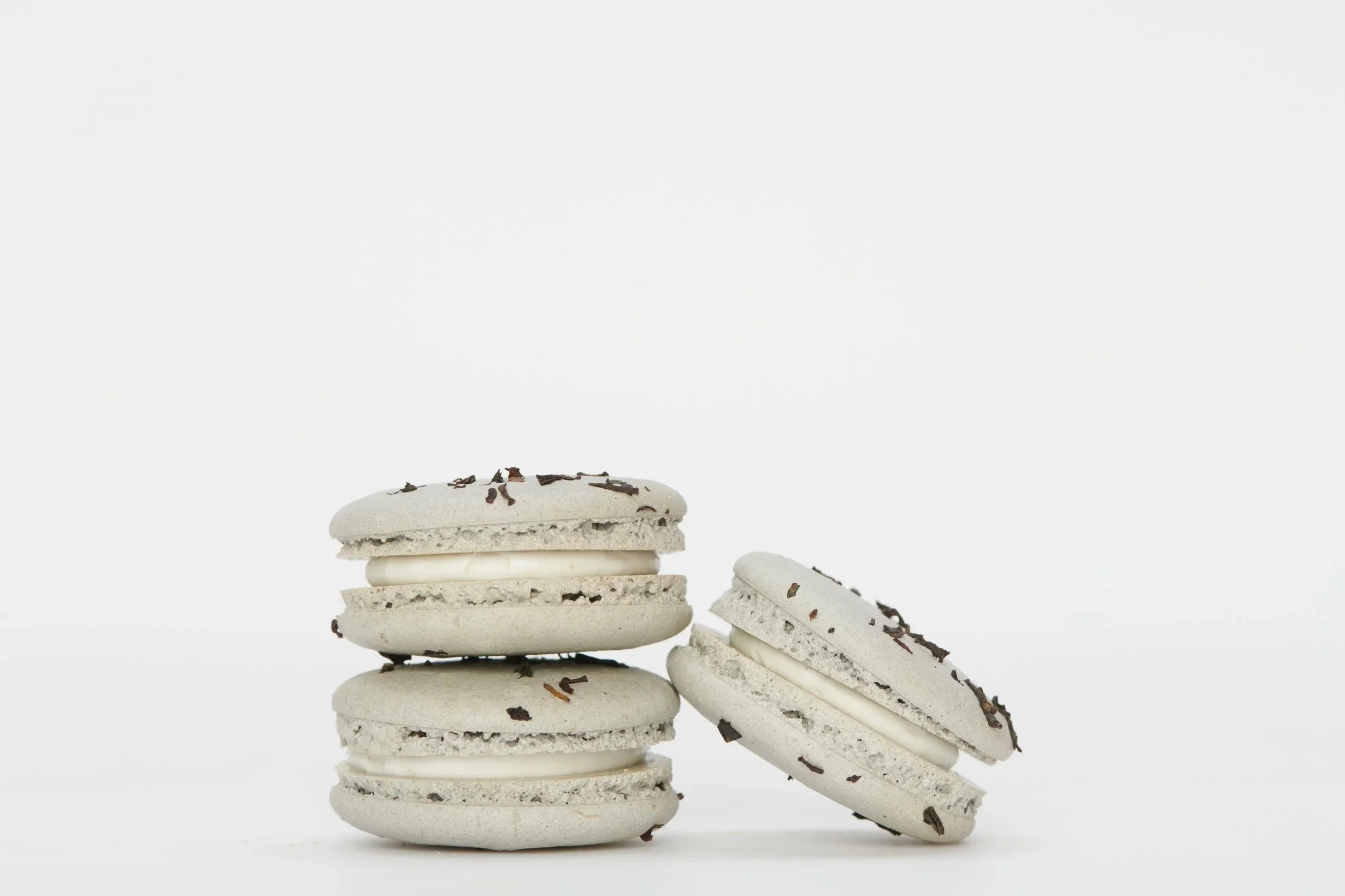 A stack of three white macarons with chocolate flakes on top, and two more macarons with filling on the side against a white background.