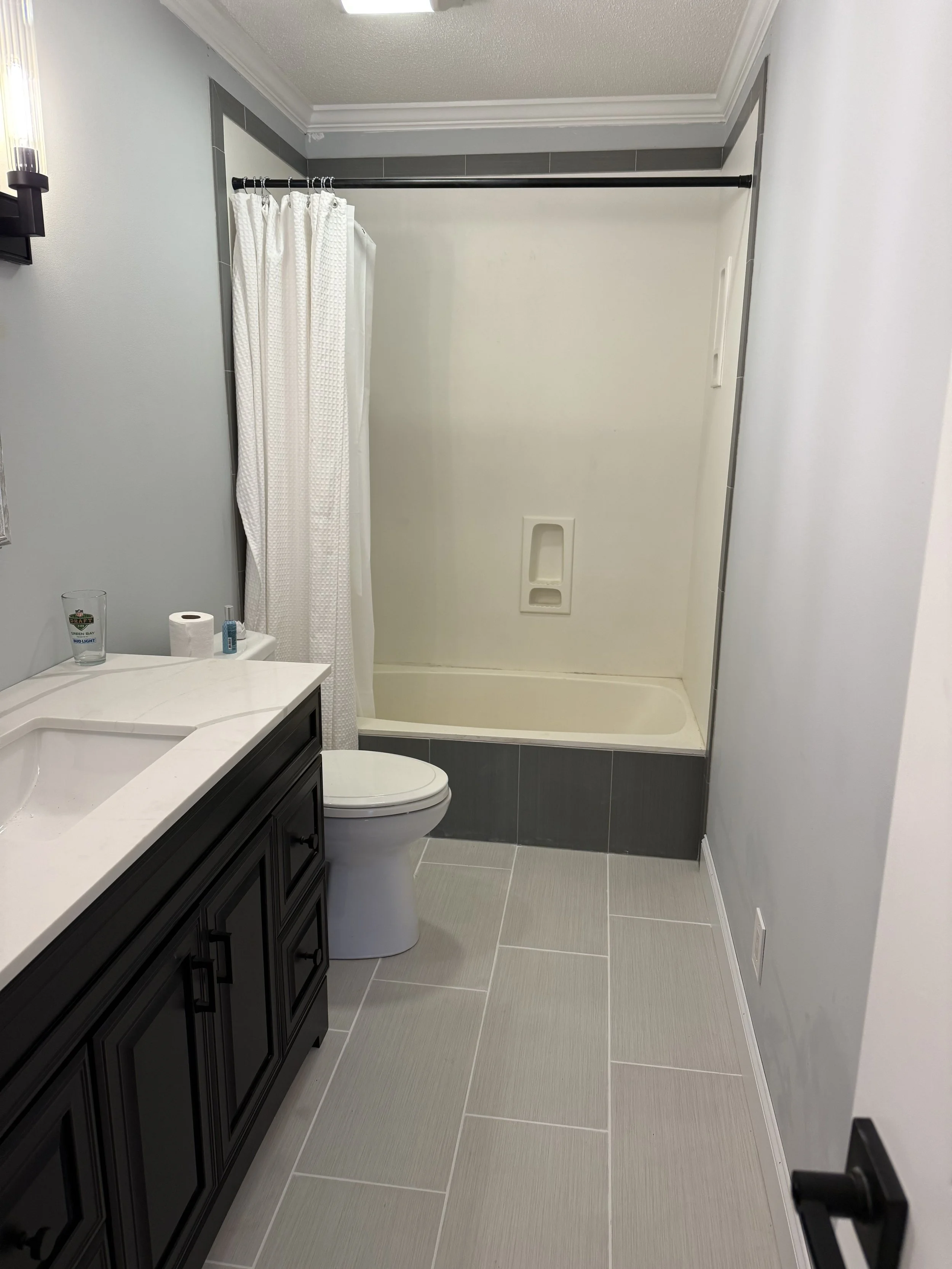 Bathroom with a shower stall, white shower curtain, dark vanity with drawers, toilet, and gray tiled floor.