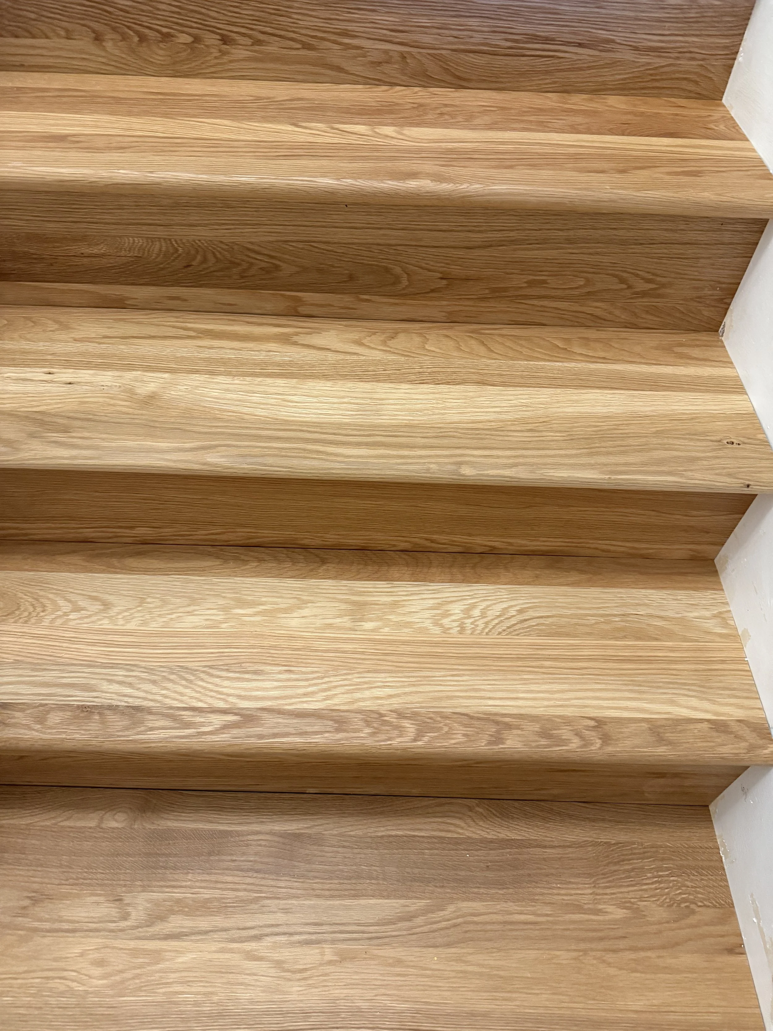 Close-up of a wooden staircase with natural white oak wood and white risers.
