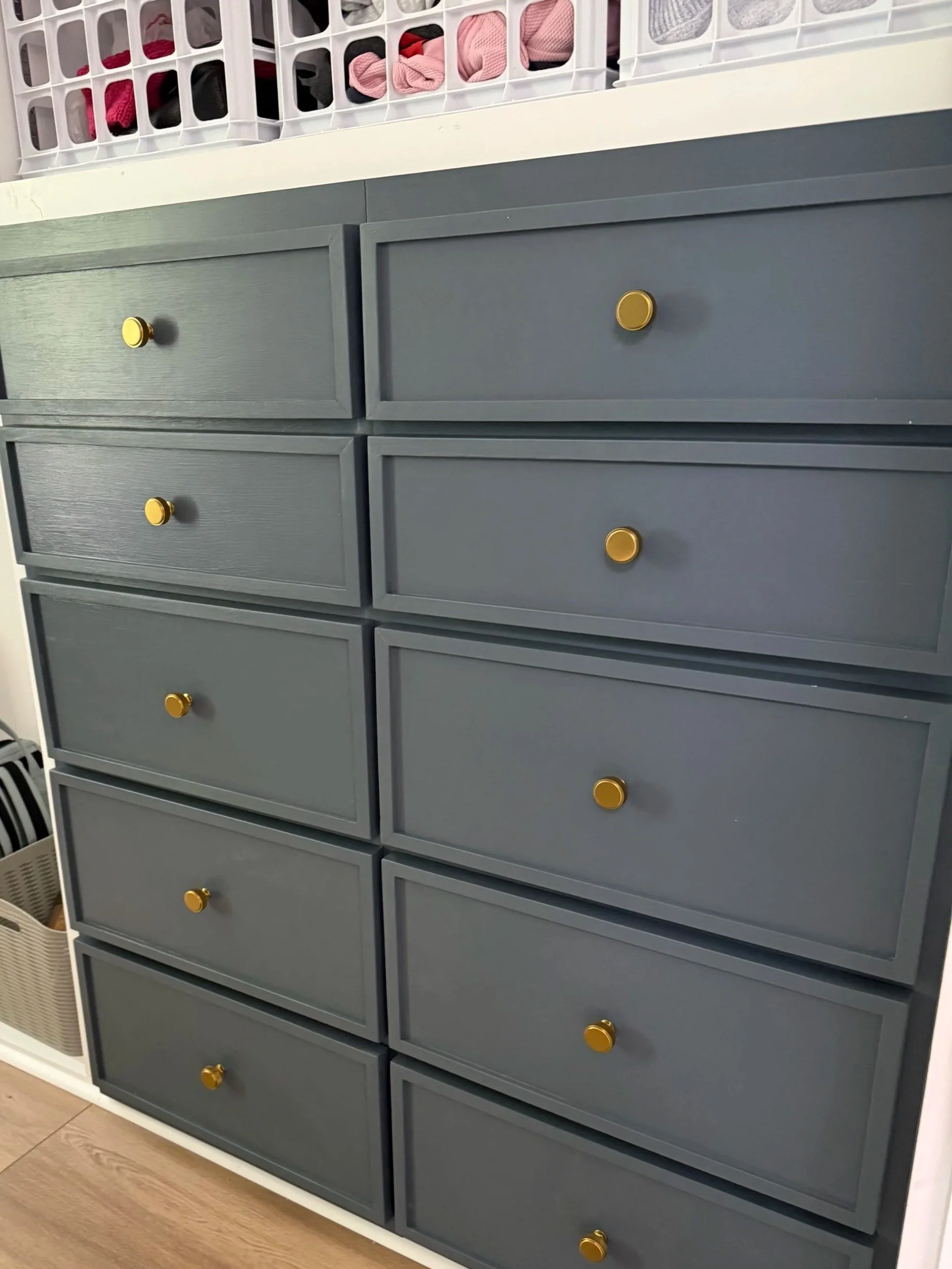 A gray dresser with multiple drawers, each fitted with round gold knobs. On top of the dresser, there is a white storage tray with compartments filled with various clothing items and socks.