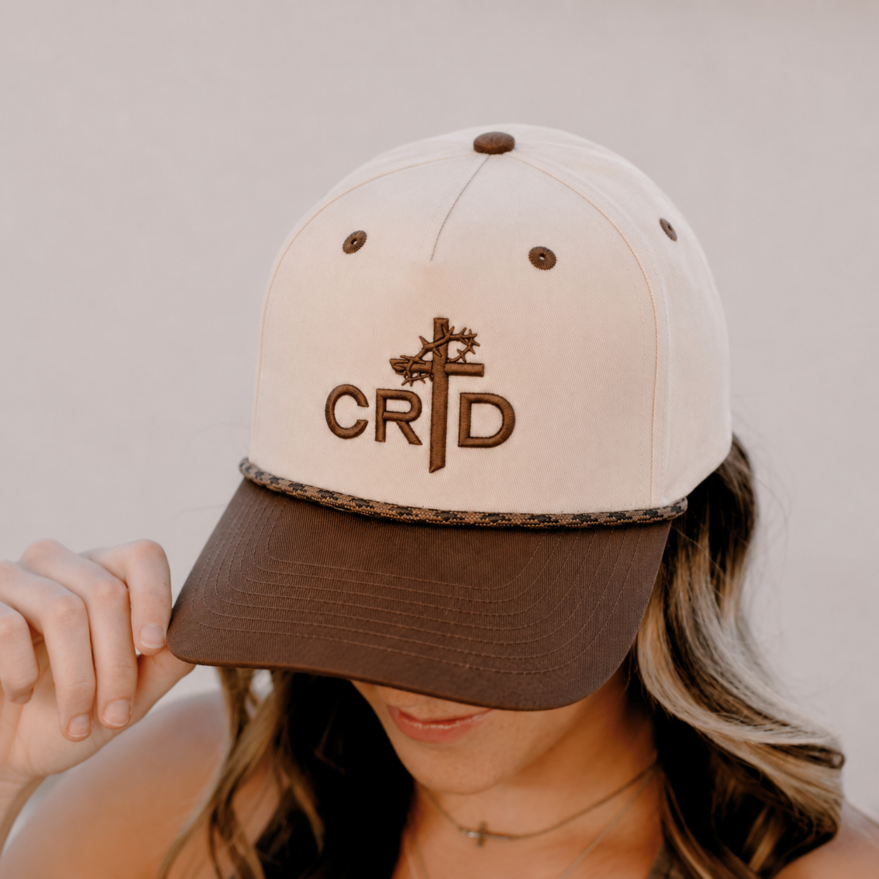 Woman wearing a beige and brown baseball cap with embroidered logo and initials.