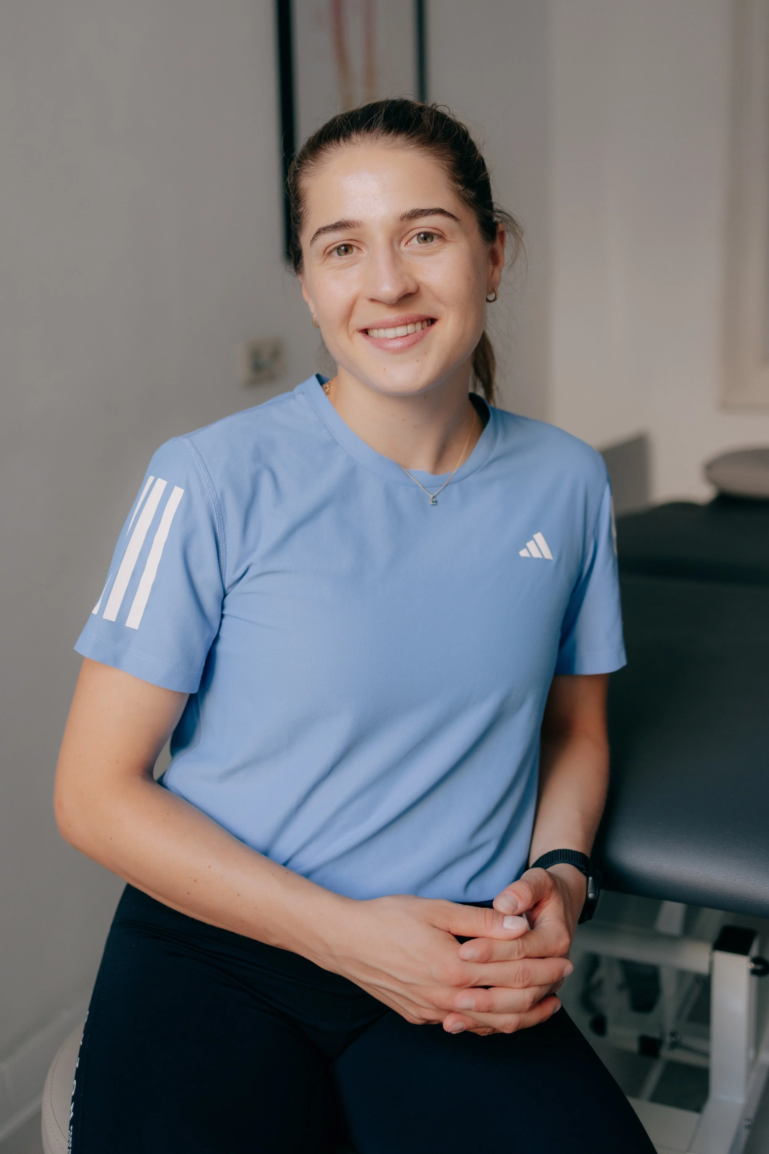 Eine junge Frau in einem blauen Sportshirt sitzt im Fitnessstudio und lächelt.