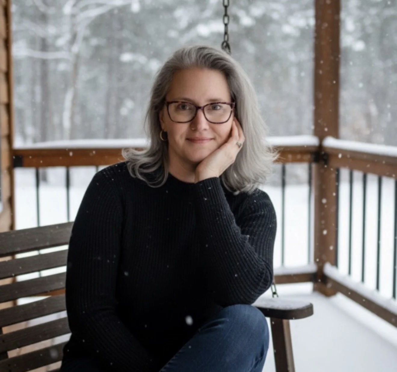 Author C. Borden sitting on a swing on a snow-covered porch, with a snowy, wooded background.